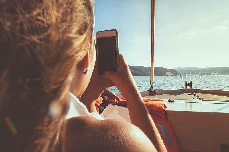 Girl taking mobile phone picture of the lake from the boat